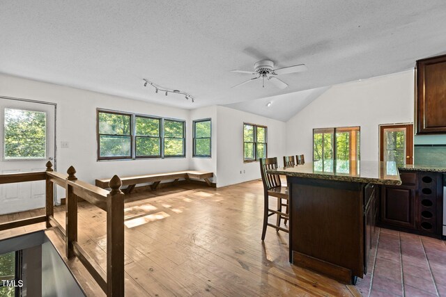 5900 Ebenezer Church Rd, Raleigh, NC 27612 - kitchen featuring a breakfast bar area, dark brown cabinetry, a ceiling fan, light stone counters, and a textured ceiling