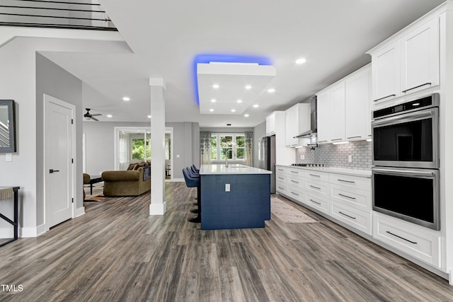 1003 E Sterlington Pl, Apex, NC 27502 - kitchen with appliances with stainless steel finishes, dark wood-style flooring, ceiling fan, wall chimney exhaust hood, and open floor plan