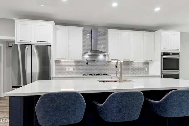 1003 E Sterlington Pl, Apex, NC 27502 - kitchen featuring wall chimney range hood, appliances with stainless steel finishes, a sink, an island with sink, and white cabinets