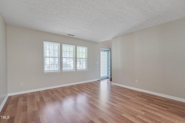 empty room with wood finished floors, a textured ceiling, and baseboards