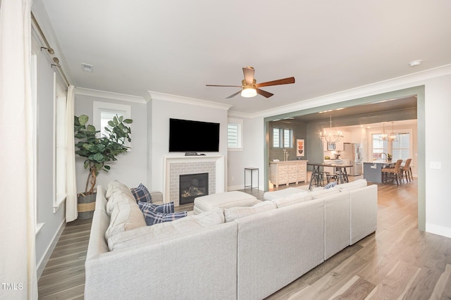 living room with crown molding, a chandelier, a fireplace, light wood-style flooring, and baseboards