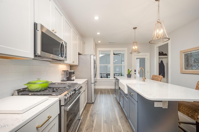 kitchen with appliances with stainless steel finishes, a sink, light wood-style flooring, white cabinets, and decorative backsplash
