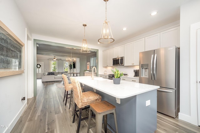 kitchen with appliances with stainless steel finishes, white cabinets, light wood-type flooring, a kitchen island with sink, and light countertops