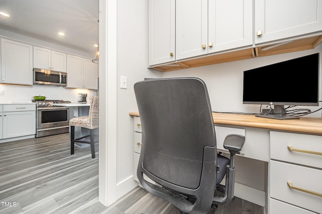 home office featuring recessed lighting, light wood-style flooring, built in desk, and baseboards