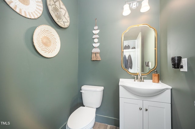 half bath featuring toilet, vanity, baseboards, and wood finished floors