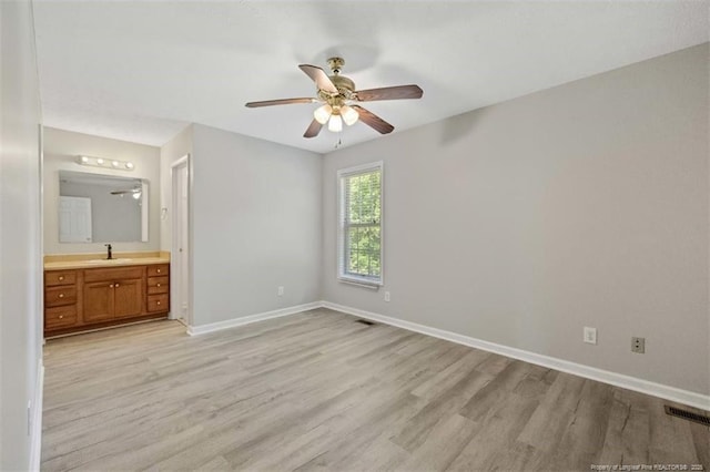 unfurnished bedroom with a sink, light wood finished floors, baseboards, and connected bathroom
