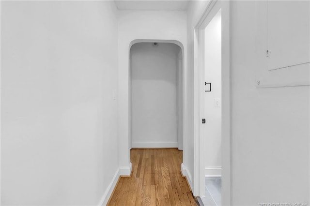 corridor featuring light wood finished floors, arched walkways, and baseboards