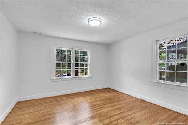 spare room with plenty of natural light, light wood-style flooring, a textured ceiling, and baseboards