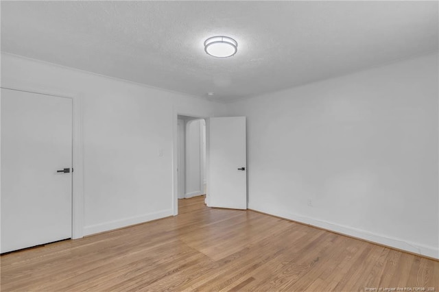 spare room with light wood-style floors, baseboards, and a textured ceiling