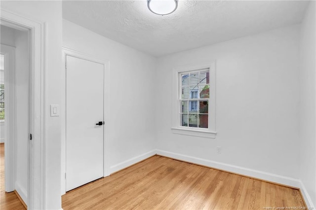 unfurnished room with light wood finished floors, baseboards, and a textured ceiling