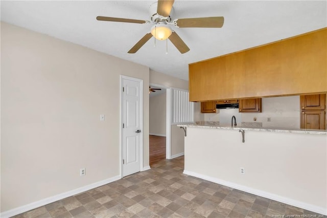 2256 Spindletree Dr, Fayetteville, NC 28304 - kitchen with under cabinet range hood, baseboards, a ceiling fan, brown cabinetry, and a kitchen bar