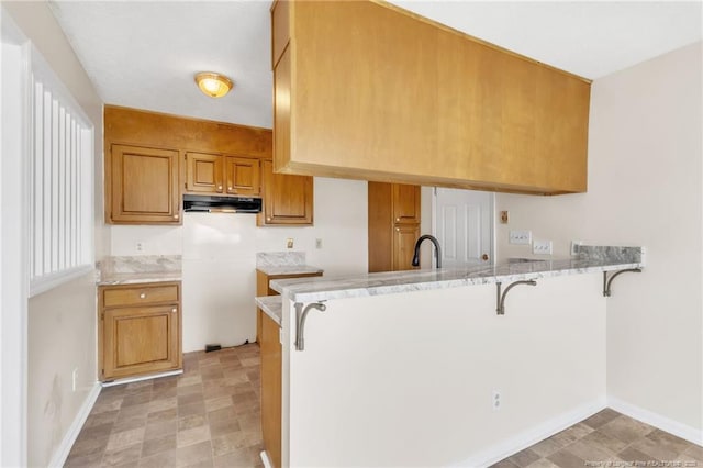 2256 Spindletree Dr, Fayetteville, NC 28304 - kitchen featuring a peninsula, a kitchen breakfast bar, brown cabinets, baseboards, and under cabinet range hood