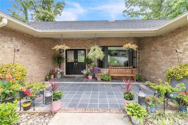 view of exterior entry with brick siding, french doors, and roof with shingles