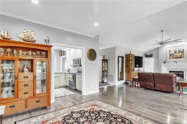 living area featuring ceiling fan, light wood-type flooring, crown molding, recessed lighting, and a fireplace