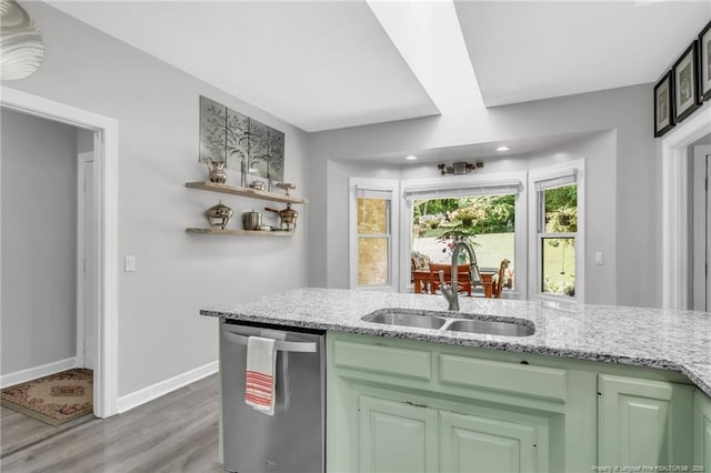 kitchen featuring stainless steel dishwasher, a sink, light wood-type flooring, light stone countertops, and baseboards