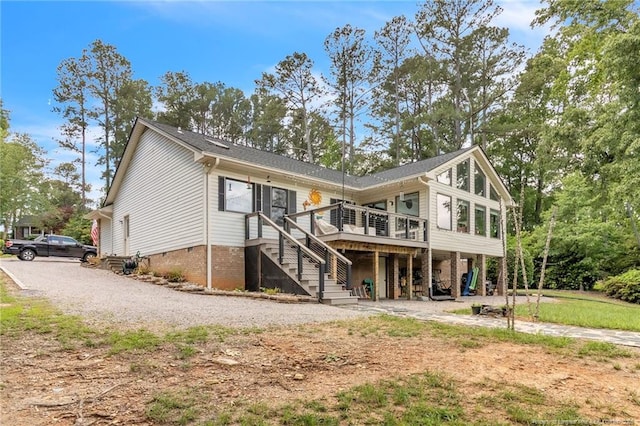 rear view of property with stairway, a deck, and gravel driveway