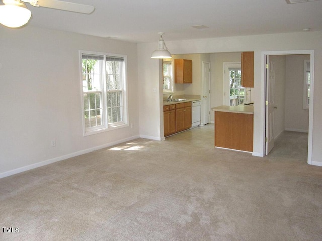 kitchen with white dishwasher, brown cabinetry, light colored carpet, a sink, and baseboards