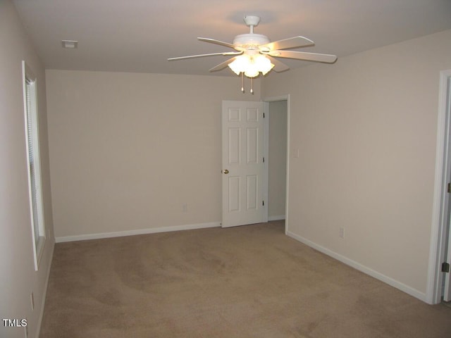 spare room featuring a ceiling fan, light colored carpet, and baseboards