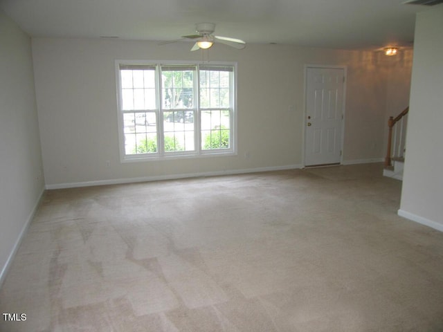 unfurnished room featuring light colored carpet, ceiling fan, baseboards, and stairs