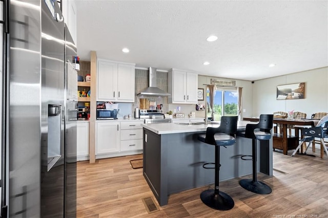 182 Ajax Dr, Saint Pauls, NC 28384 - kitchen featuring appliances with stainless steel finishes, wall chimney range hood, a sink, white cabinets, and light wood-style floors
