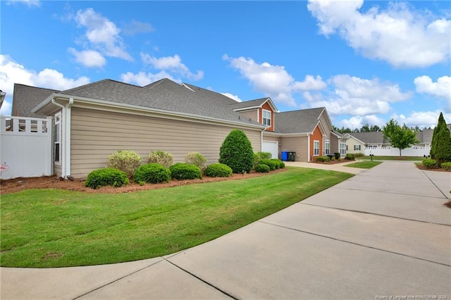 view of side of home featuring a lawn, concrete driveway, an attached garage, and a residential view