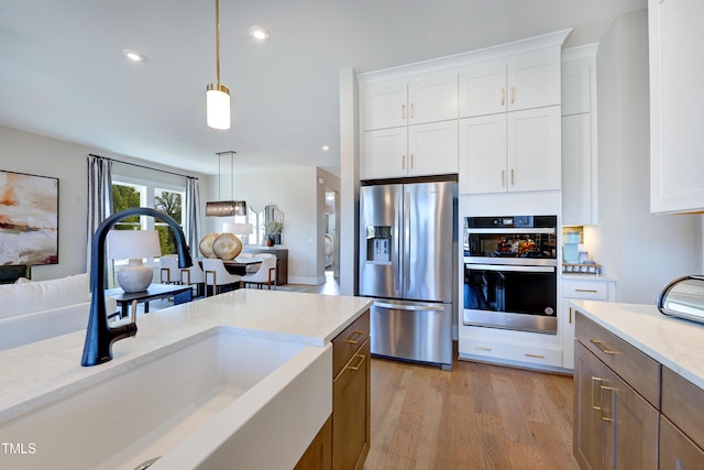 kitchen with stainless steel appliances, a sink, pendant lighting, white cabinets, and recessed lighting