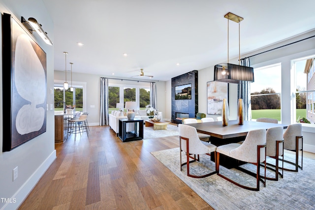 dining room featuring a ceiling fan, light wood finished floors, baseboards, a fireplace, and recessed lighting