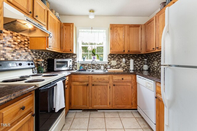 kitchen with white appliances, under cabinet range hood, a sink, tasteful backsplash, and light tile patterned floors