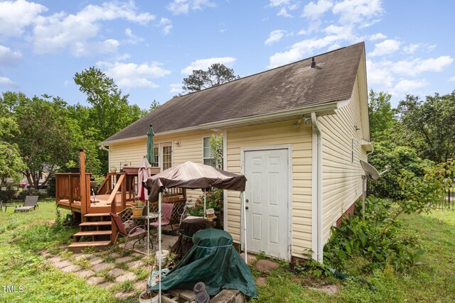 rear view of property featuring a deck, roof with shingles, an outbuilding, and a storage shed