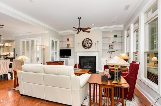 241 Serenity Hill Cir, Chapel Hill, NC 27516 - living room with a ceiling fan, built in features, a glass covered fireplace, wood finished floors, and crown molding