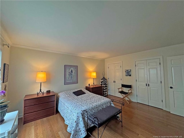 bedroom featuring multiple closets, ornamental molding, light wood-style flooring, and baseboards