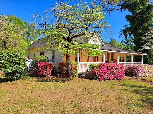 view of front facade featuring covered porch, a front yard, and a chimney