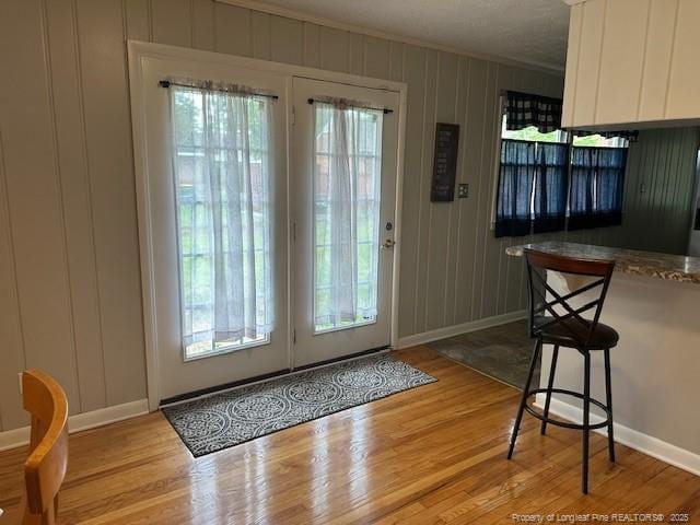 doorway to outside with baseboards, crown molding, light wood-style flooring, and a decorative wall