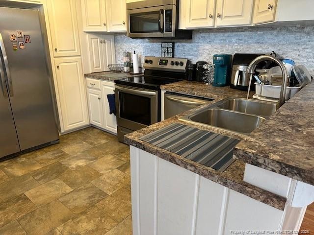 kitchen with stainless steel appliances, dark countertops, decorative backsplash, and a sink
