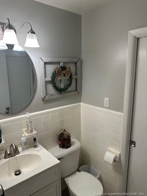 bathroom featuring tile walls, toilet, vanity, and a wainscoted wall