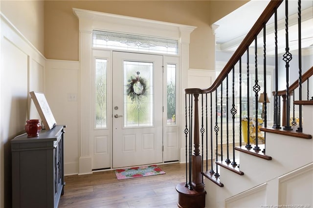entrance foyer featuring a decorative wall, wood finished floors, stairway, and a wainscoted wall