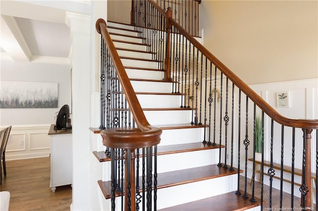 stairs featuring a wainscoted wall, wood finished floors, a decorative wall, and ornamental molding