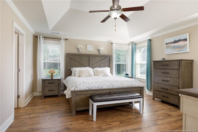 bedroom with crown molding, wood finished floors, a tray ceiling, baseboards, and ceiling fan