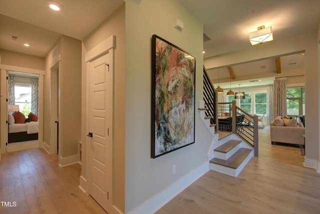 corridor with light wood finished floors, healthy amount of natural light, stairs, baseboards, and recessed lighting