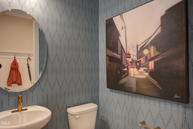 half bathroom featuring a sink, wallpapered walls, and toilet