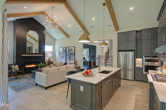 kitchen featuring appliances with stainless steel finishes, light wood-type flooring, a sink, light stone countertops, and beam ceiling