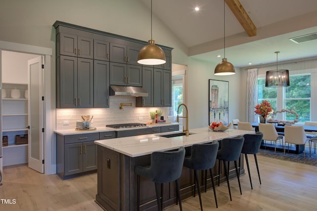 kitchen featuring a sink, under cabinet range hood, gray cabinets, stainless steel gas cooktop, and light wood finished floors