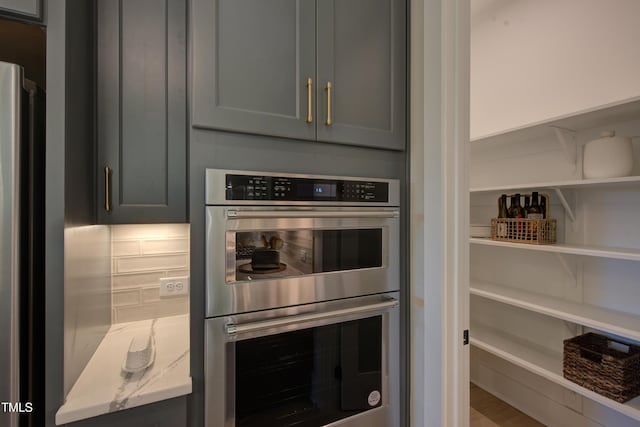 kitchen view of stainless steel double oven, gray cabinetry, and backsplash