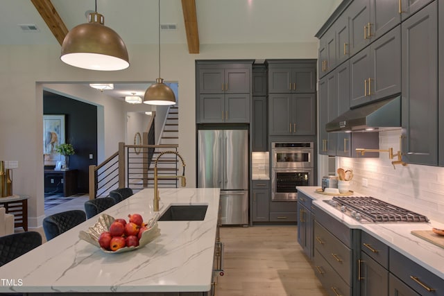 kitchen featuring appliances with stainless steel finishes, under cabinet range hood, beamed ceiling, tasteful backsplash, and light wood-type flooring