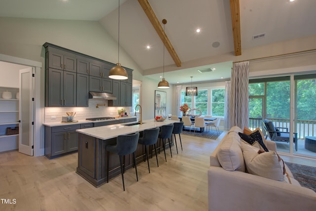 kitchen with under cabinet range hood, a sink, a breakfast bar, stainless steel gas cooktop, and gray cabinetry
