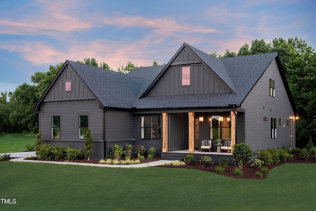 view of front facade featuring board and batten siding, covered porch, a yard, and a shingled roof