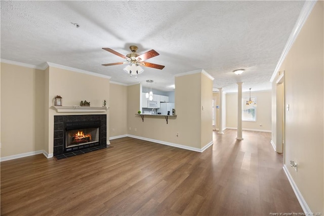 unfurnished living room featuring dark wood-type flooring, ceiling fan, ornate columns, a tile fireplace, and a textured ceiling