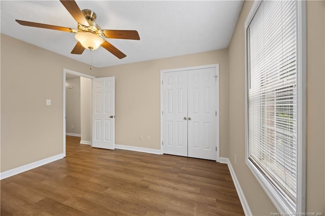 unfurnished bedroom featuring wood finished floors, baseboards, a closet, and ceiling fan