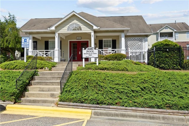 view of front of house with covered porch, uncovered parking, fence, and stairs