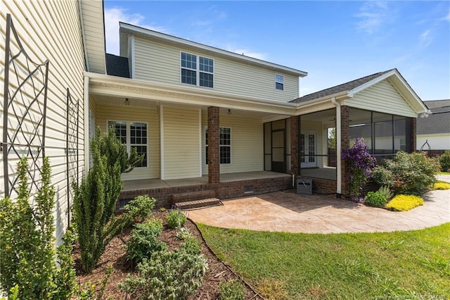 rear view of house with a sunroom, a patio area, and a lawn